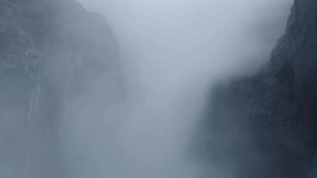 Dense mist spreads through a steep mountain gorge between dark rocky cliffs