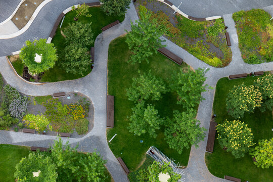 Top view of a landscaped urban park with green lawns, trees, flower beds, curved paths and benches. Modern public green space combining nature, recreation and landscape design.