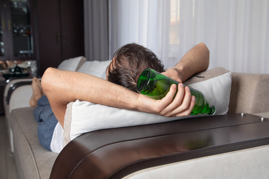 Caucasian man with a bottle of beer lying on sofa.