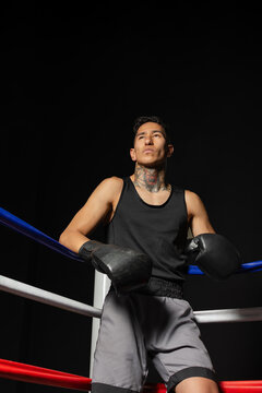 Relaxed Hispanic boxer leaning on ring ropes against black background