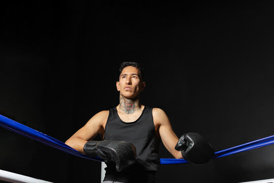 Calm Hispanic boxer standing in boxing ring corner against dark background