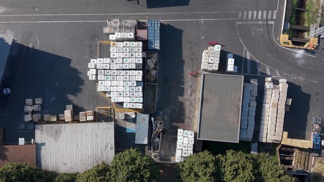 Aerial view of a manufacturing facility with stacked chemical containers, pallets, and industrial storage areas in Milan, Lombardy, Italy.