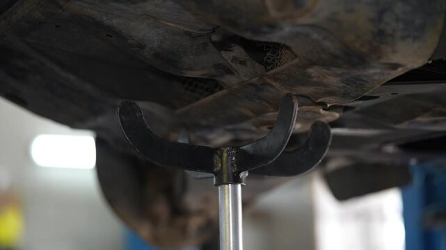 A metal hydraulic transmission jack stand supporting an underbody component or subframe of a car raised on a lift.