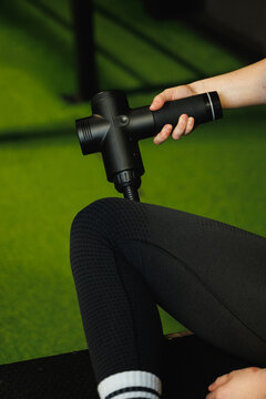 Person uses a handheld massage gun on a leg, photographic style, green gym background, exercise recovery and muscle care