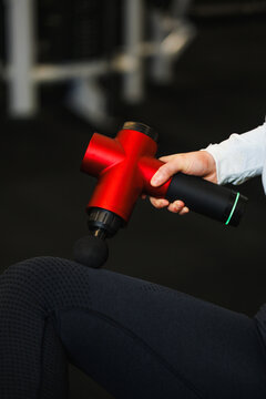 Person using a red percussion massage gun on leg muscles, realistic photo style, dark background, recovery concept