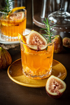 Craft fig cocktail garnished with fresh rosemary sprig and sliced fig in a glass on a dark rustic table. Gourmet bourbon drink with orange peel twist for autumn season menu concept. 