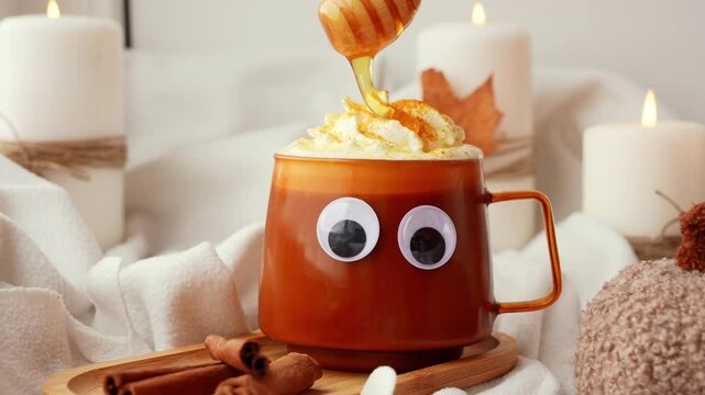 Pouring honey Seasonal drink cacao coffee with whipped cream and cinnamon sticks Halloween funny face on cup Hello Fall Halloween concept. Celebrating autumn holidays at cozy home on the windowsill