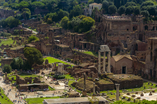 View of the ancient Roman Forum ruins with stone columns, historic brick structures, and tourists walking along pathways in Rome, Lazio, Italy.