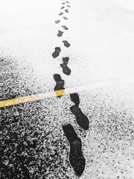 Footprints in the Snow Walking Across Parking Lot with Yellow Lines on Street
