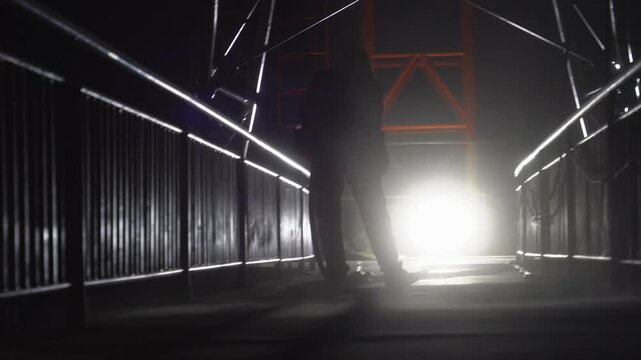 Silhouette of Industrial Worker Sandblasting Walkway at Night Against Bright Backlight