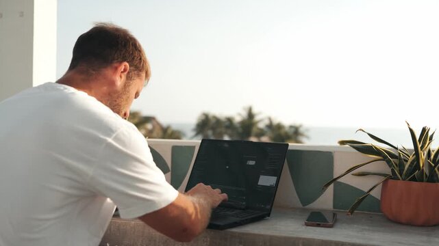 Digital nomad freelancer working on his laptop from a tropical balcony with a sea view in mexico