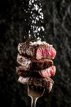 A stack of perfectly grilled medium rare beef steak pieces on a fork with sea salt falling from above