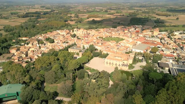Aerial view of the historic Peralada Castle surrounded by lush gardens and the terracotta rooftops of the town in Peralada, Catalonia, Spain.
