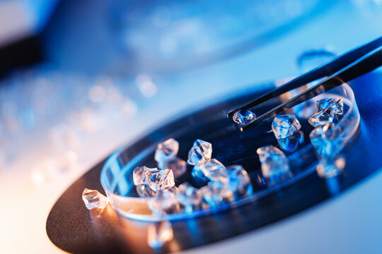Angled closeup of laboratory diamonds in petri dish with tweezers for lab factory background