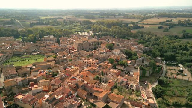 Aerial view of the historic town of Peralada, featuring dense terracotta rooftops, narrow stone streets, and surrounding lush greenery in Peralada, Catalonia, Spain.