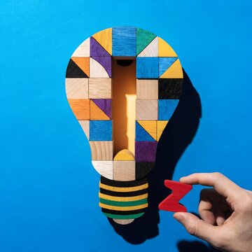Light bulb innovation concept with colorful wooden geometric blocks arranged on bright blue background hand holding red zigzag block symbolizing creative ideas and logical thinking artwork  generated 