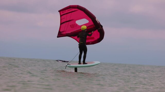 An athlete standing on the board holds on to the wing, in which the wind creates thrust in slow motion. Wingfoil board where a surfer glides through the water on a hydrofoil board.