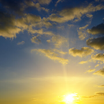 Scenic Dramatic Sunrise with Sunbeams Breaking Through Cumulus Clouds. Vibrant Blue and Yellow Celestial Texture for Natural Backgrounds and Design.
