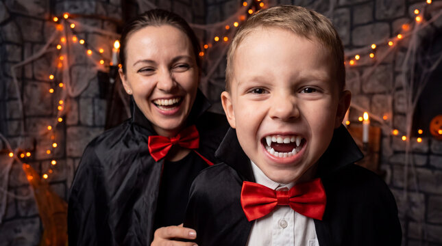 Mother and son in cute vampire costumes making funny fang faces at camera for Halloween, ideal for spooky family party invitations and marketing banners.