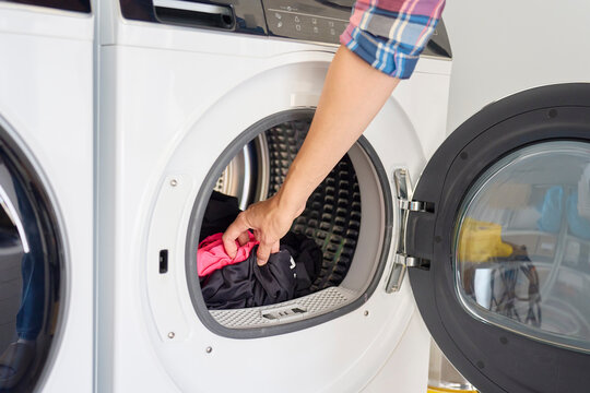Woman removing clothes from open tumble dryer after drying cycle