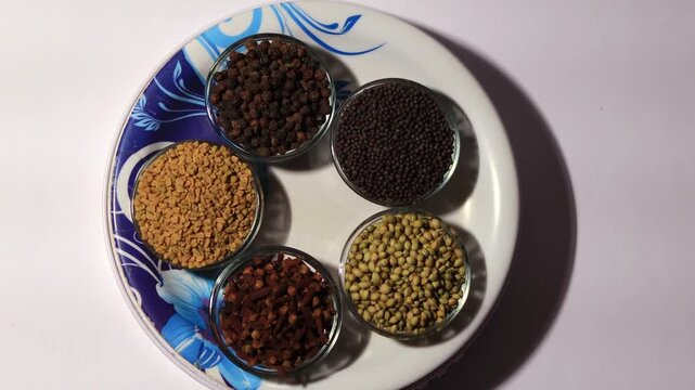 Set of dried Indian spices in serving plate and glass bowl table top view spin.