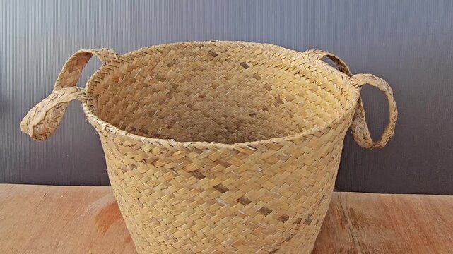 empty basket on wooden background Handwoven basket rests on wooden surface. Natural fibers form rustic, textured pattern. Four handles looped for easy carrying. Soft golden tones match warm wood grain