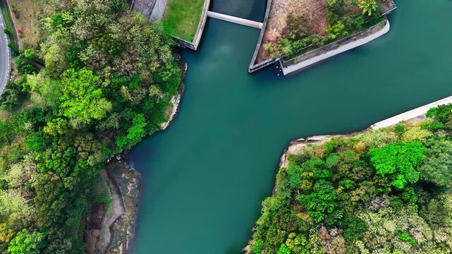 Aerial view of the PLTA Sengguruh hydroelectric power plant surrounded by lush green forests and river water in Malang, East Java, Indonesia.