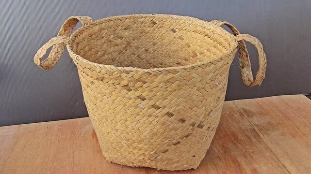 empty basket on wooden table,Handwoven basket rests on wooden surface. Natural fibers form rustic, textured pattern. Four handles looped for easy carrying. Soft golden tones match warm wood grain. 