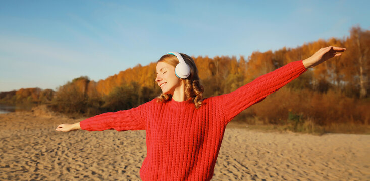 Happy young woman enjoying listening to music in headphones outdoors in autumn park
