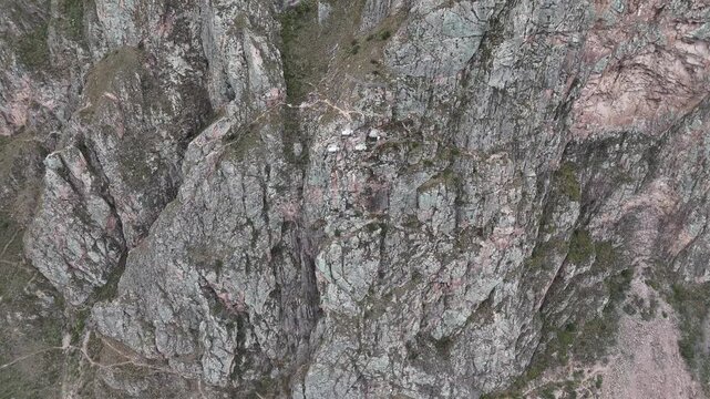 Cinematic close-up aerial view of a steep rock wall featuring unique hanging hotel capsules in Peru.