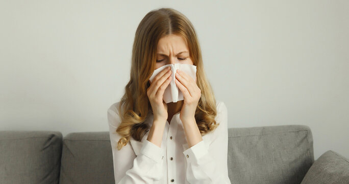 Sick exhausted young woman sneezing blow nose using tissue, unhealthy suffering girl feels unwell