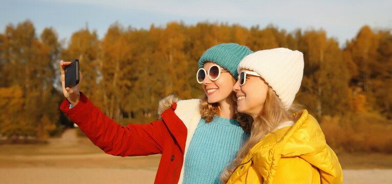 Happy young women friends with smartphone together on beach, smiling girlfriends using phone on sea