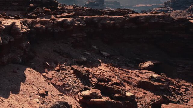 The scene shows a rocky terrain in a canyon. The ground is made of various stones and rocks. Sunlight casts shadows on the surfaces. The steep walls of the canyon rise in the background.