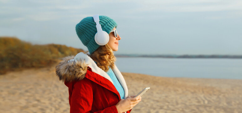 Happy young woman enjoying listening to music in headphones with phone outdoors in autumn park