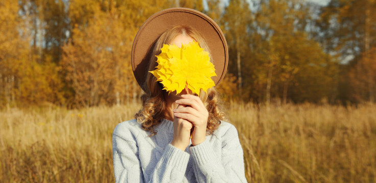 Happy cheerful woman having fun with yellow maple leaves in autumn park, nature background