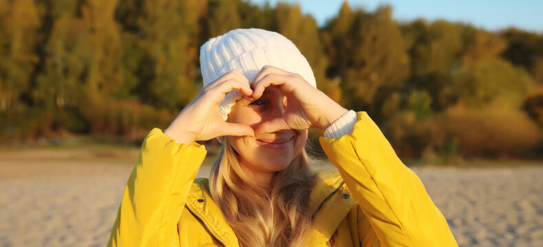 Happy woman showing heart shaped sign gesture with hands in autumn park