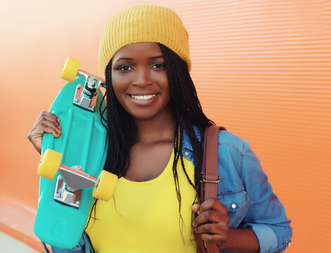 Summer portrait of stylish happy African young woman with skateboard, modern black teenage girl