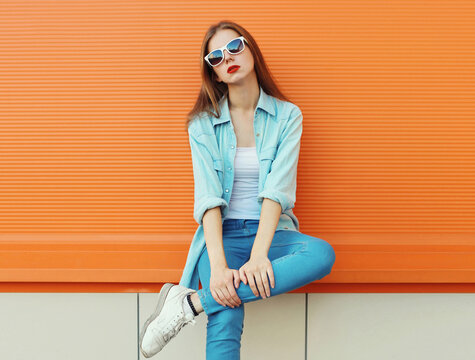 Portrait of modern stylish young woman in white glasses, casual clothing posing on orange background