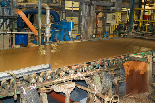 Wet pulp mixture flows over industrial rollers on a metal conveyor belt system inside a large recycling facility during standard daily operation
