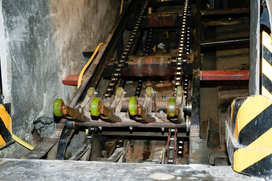 Heavy machinery with iron chains and green rollers pulls scrap cardboard through a narrow channel for efficient recycling at a waste treatment center