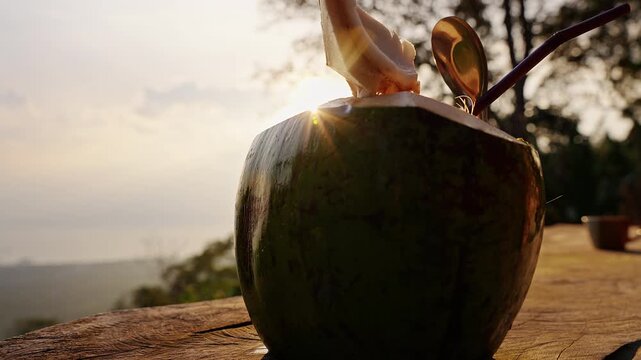 Fresh Coconut Drink With Straw and Spoon Rests on a Rustic Wooden Table at Sunset, Showing Tropical Refreshment and Natural Wellness