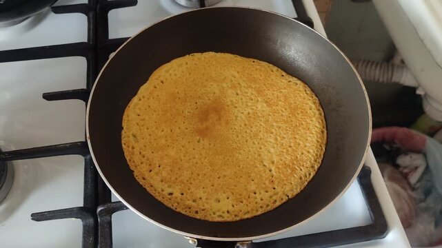 Golden crepe with porous texture frying in a black pan on a gas stove top view