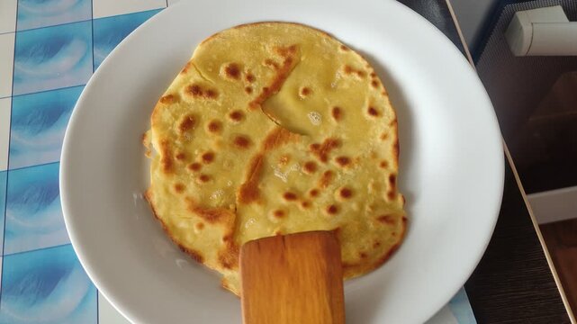 Large golden fried flatbread pancake served on a white plate with wooden spatula