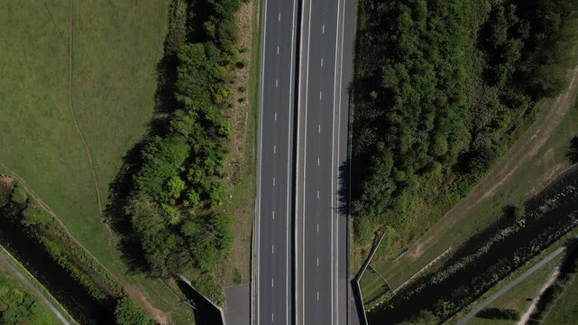 Aerial view of a highway bridge crossing over a canal with green fields and trees in Lancaster, England, United Kingdom.