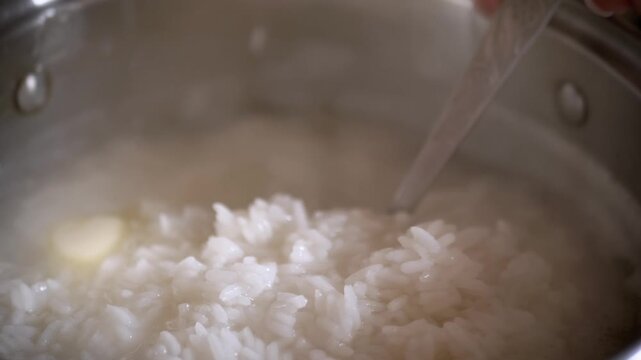 Close-up of hot cooked white rice being scooped with a metal spoon from a boiling pot. Concept of traditional home cooking, healthy carbohydrate source, and culinary staples.