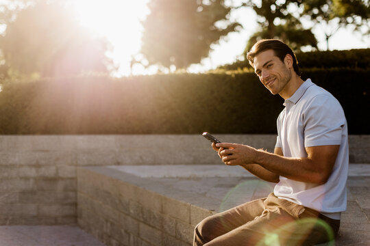 Smiling man enjoying a sunny afternoon while using his smartphone