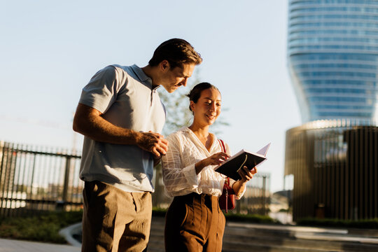 Couple exploring a sunny urban park while sharing a notebook