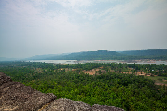 Scenic high angle view of lush green forest, wide river, and distant mountains under a cloudy sky from a cliff edge,A breathtaking high angle panoramic view overlooking a vast lush green tropical fore