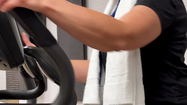 Individual engages in exercise on elliptical machine at a gym. Towel rests on shoulders as they focus on fitness routine.