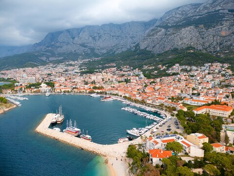 An aerial top-down view highlights luxury yachts and motorboats moored in orderly rows within a turquoise marina along the Adriatic coast in Dalmatia